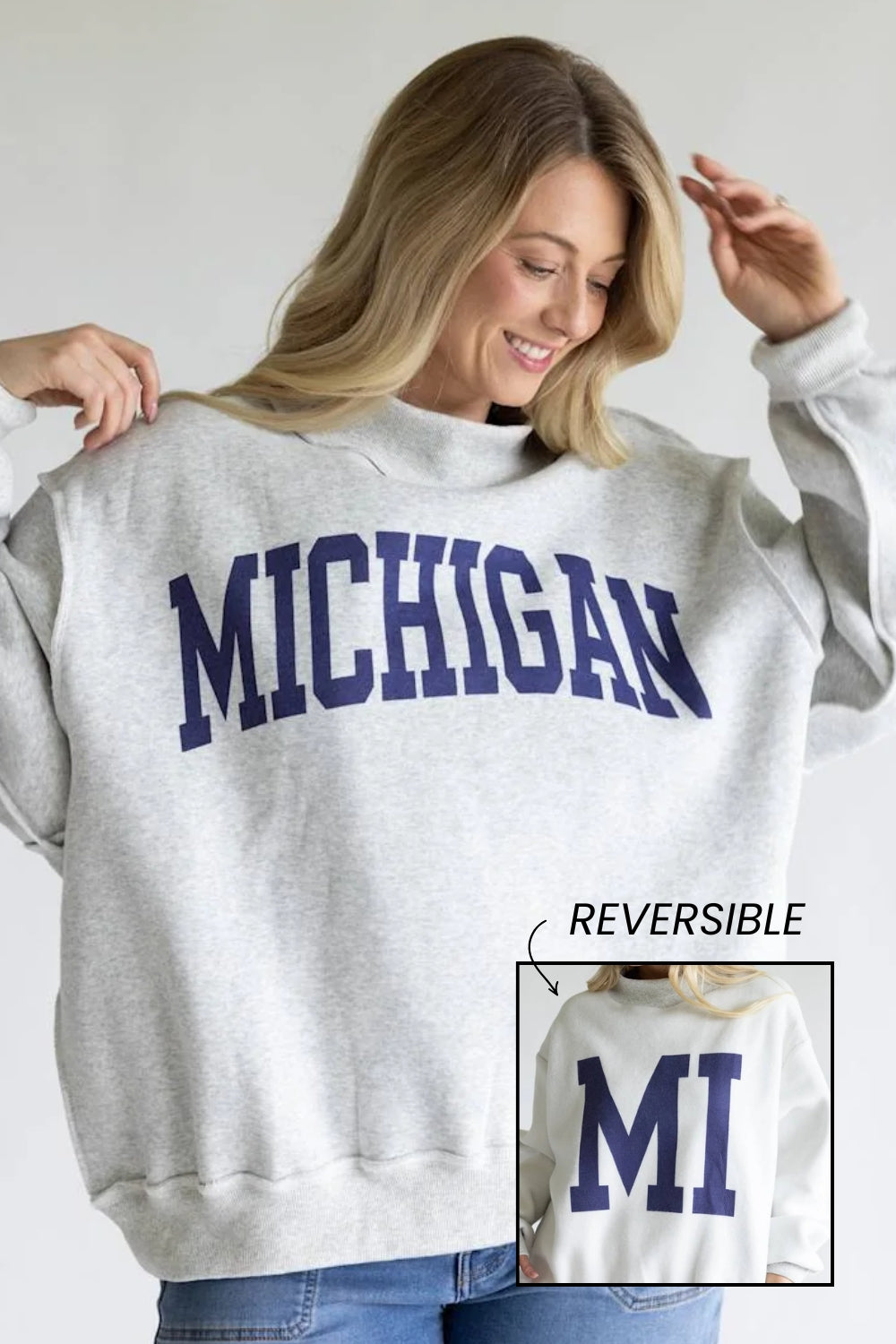 A woman wearing a light heather gray sweatshirt with 'MICHIGAN' printed in navy blue across the chest. The image includes a small inset showing the reverse side of the sweatshirt with 'MI' printed in navy.