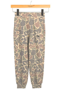 A pair of jogger-style pants with an abstract organic camouflage pattern in beige, brown, and gray, hanging from a wooden hanger against a white background.