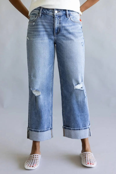 Front view of a model wearing light-wash cropped wide-leg jeans with distressed knee details and cuffed hems, paired with white woven slip-on flats against a neutral gray background.