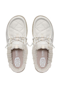 A pair of HEYDUDE slip-on shoes in off-white, featuring quilted leather uppers, white faux-fur lining, braided laces, and a visible HEYDUDE logo on the insole, shown from a top-down view on a white background.